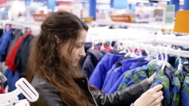 young woman chooses jacket on child in clothes store