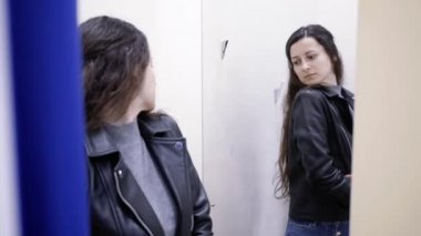 Genç bir kadın, elbise mağazasında deri ceket denedi.