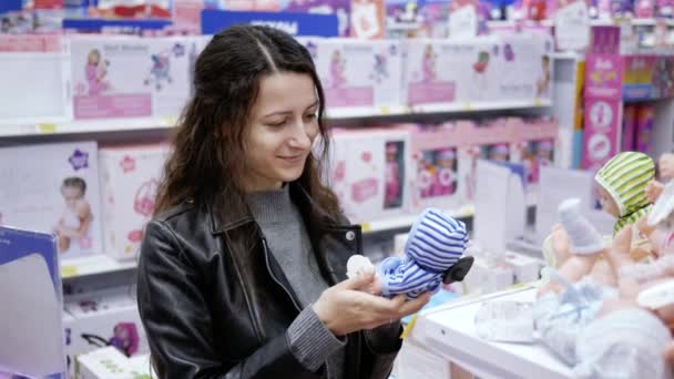 Young woman choose a toy doll in a children 's store for my daughter — стоковое видео