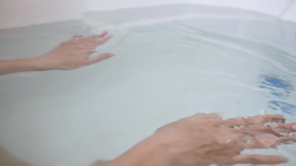 Primer plano de las manos de la mujer en la bañera llena de agua. Levanta sus manos en el agua — Vídeos de Stock