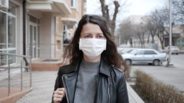 Koruyucu tıbbi maskeli genç bir kadın şehirde dolaşıyor. Ağır çekim. Koronavirüs