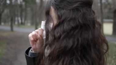 Şehirde yürüyen koruyucu maskeli genç bir kadının portresi. Öksürük. Pandemik koronavirüs