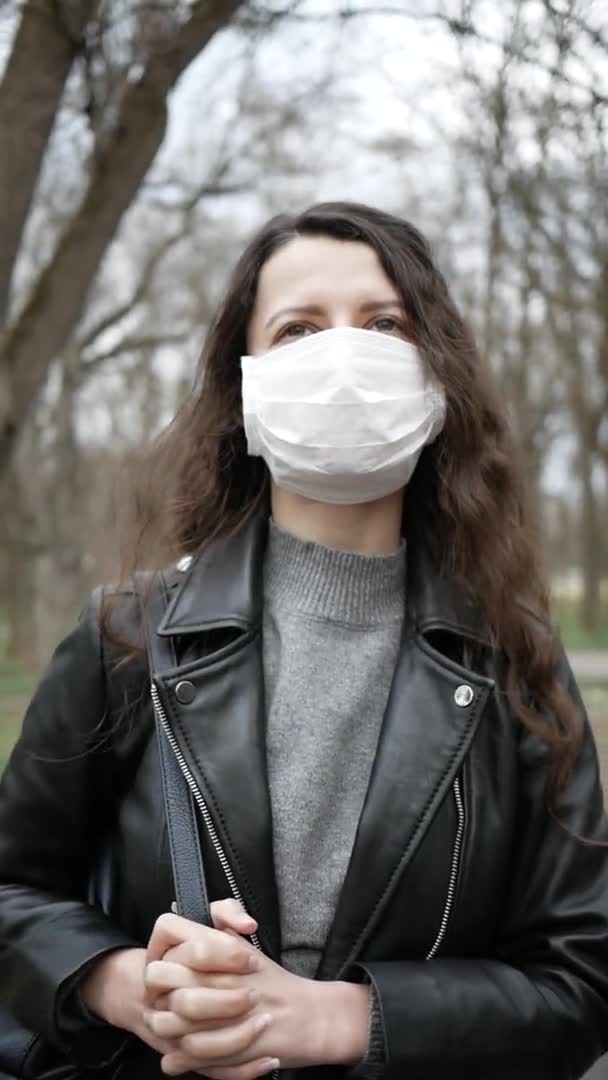 マスクの若い女性は街の公園にいる。パンデミックコロナウイルス。垂直ビデオだ。スローモーション — ストック動画