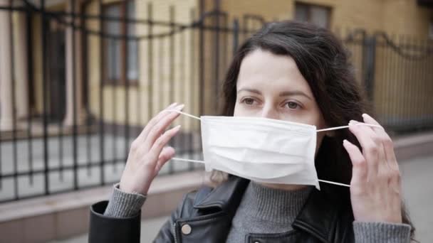 Jonge vrouw zet masker op voor bescherming tegen coronavirus COVID-19. Portret van een meisje met een beschermend masker in de stad — Stockvideo