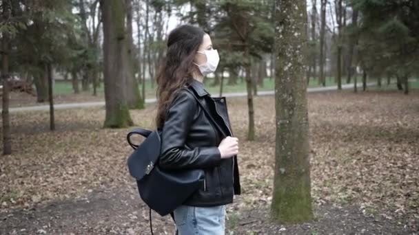 Mooie jonge vrouw loopt op het stadspark met een beschermend masker. Pandemisch coronavirus — Stockvideo