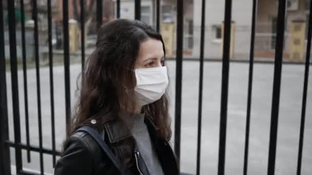 Jonge vrouw met medisch masker op haar gezicht loopt in de stad. Volwassen vrouw bedekt haar gezicht met masker om jezelf te beschermen tegen ziekten — Stockvideo