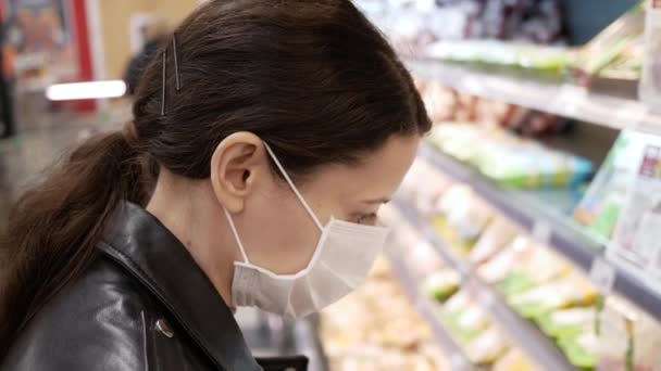 Hermosa morena joven en máscaras médicas en la tienda de comestibles. pandemia. Selecciona productos — Vídeo de stock
