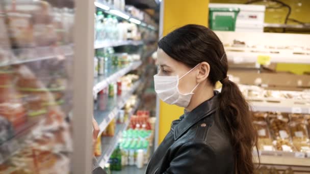 Bela morena jovem em máscaras médicas no supermercado. pandemia. Seleciona produtos — Vídeo de Stock