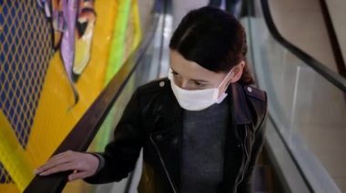 Koruyucu maskeli bir mağazada genç bir kadın. Yürüyen merdivende yükseliyor.