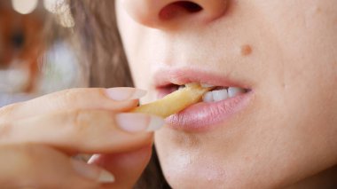 Tanınmayan genç bir kadın fast food restoranında patates kızartması yiyor. Bir eli patatesli, ağzı kapalı..