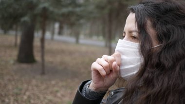 Şehirde yürüyen koruyucu maskeli genç bir kadının portresi. Öksürük. Pandemik koronavirüs.