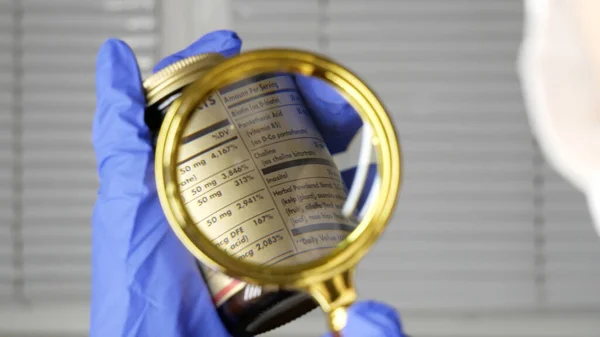 Investigating ingredients of medicines, chemicals used in pills capsules inside box using magnifying glass, gloved hand.