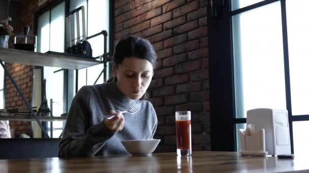 Linda jovem mulher feliz sentada à mesa no café e desfrutando da refeição. Mulher com fome atraente comendo almoço saboroso — Vídeo de Stock