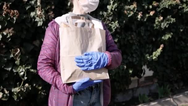 Consegna cibo giovane donna in maschera protettiva e guanti porta borsa con prodotti dal negozio. pandemia — Video Stock