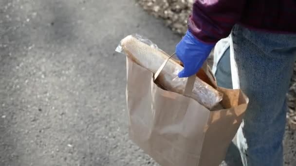 Essensausgabe junge Frau in Schutzmaske und Handschuhen trägt Tasche mit Produkten aus dem Geschäft. Pandemie — Stockvideo