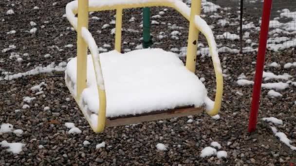 Balanço vazio a balançar na neve. Um parque infantil vazio — Vídeo de Stock