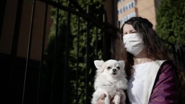Portret van jonge vrouw met medisch masker en haar hond Chihuahua loopt op straat tijdens pandemische corona virus — Stockvideo
