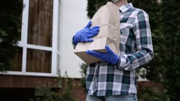 Correio, homem de entrega em máscara protetora e luvas médicas entrega comida takeaway. Serviço de entrega sob quarentena, surto de doença, coronavírus covid-19 condições pandêmicas. Fica em casa. — Vídeo de Stock