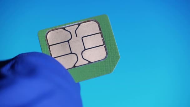 Рука крупным планом в синих перчатках держит зеленую микро SIM-карту на синем фоне. Концепция инженера по оборудованию связи на заводе — стоковое видео