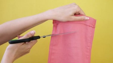 Yakın plan genç kadın ucube sarı arka planda izole edilmiş, pembe kot pantolon ve makas kesiyor. 4K