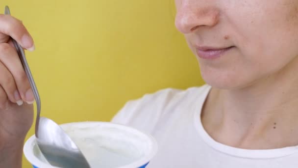 Il primo piano di bella giovane donna attraente mangia lo yogurt da un cucchiaio. Su sfondo giallo isolato. 4K — Video Stock