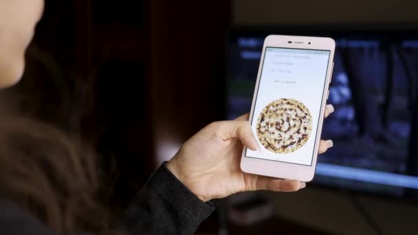 Выберите Поиск доставки пиццы через Интернет в мобильном приложении с помощью мобильного телефона. Крупный план экрана смартфона и женских пальцев дома — стоковое видео