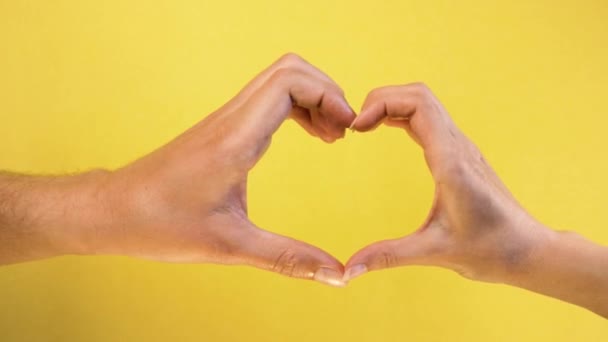 Heart shaped from fingers. Male and female hand isolated on yellow background. concept of Valentine day — Stock Video