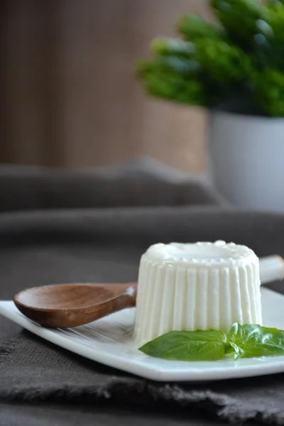 Queso fresco con hojas de albahaca en un plato blanco y una mesa con — Foto de Stock