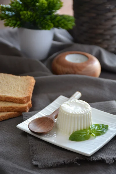 Verse kaas met basilicum bladeren op een witte plaat en een tafel met — Stockfoto