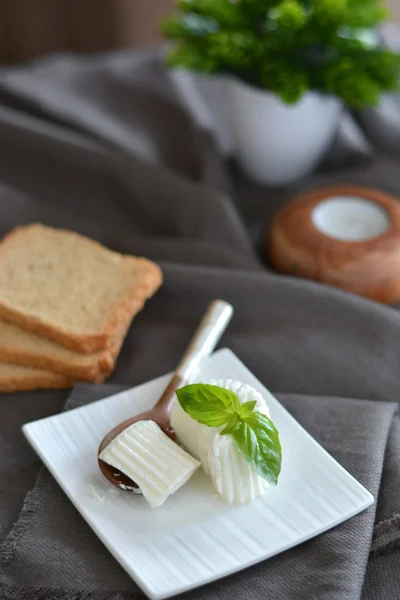 Queijo fresco com folhas de manjericão em um prato branco e uma mesa com — Fotografia de Stock