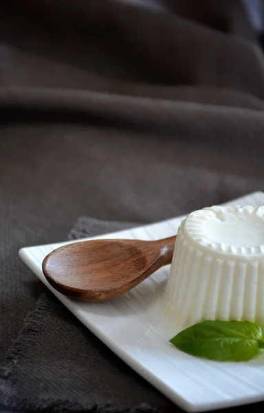 Queso fresco con hojas de albahaca en un plato blanco y una mesa con — Foto de Stock