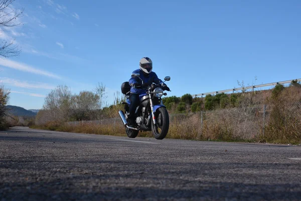 Motociclista com capacete azul passando por uma estrada — Fotografia de Stock