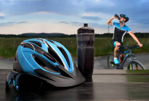Helm dan kacamata hitam pengendara sepeda dengan jalan dan pengendara sepeda akan melalui — Stok Foto
