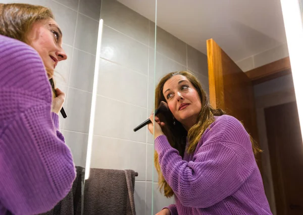 40歳の女性が化粧をし 仕事に行く前にバスルームで彼女の肌の世話をする ロイヤリティフリーのストック画像
