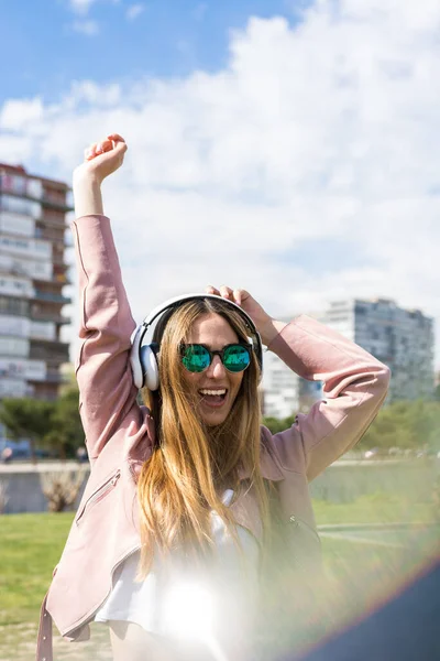 若い幸せな女の子は春の日に彼女のヘッドフォンで音楽を聴きながら踊っています — ストック写真