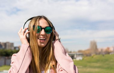 Genç ve mutlu kız bir bahar günü kulaklıkla müzik dinlerken dans ediyor.