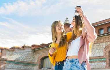 İki mutlu arkadaş sokakta yürürken birbirlerine sarılıyorlar ve kahve içiyorlar.