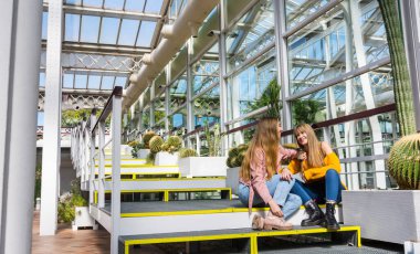 İki arkadaş parkta yürürken birbirlerine sırlarını anlatırken gülüp fotoğraf çekiyorlar.