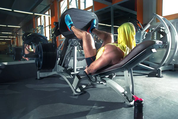 Fitness and Sport. Athletic man doing exercises on legs in gym among other people.