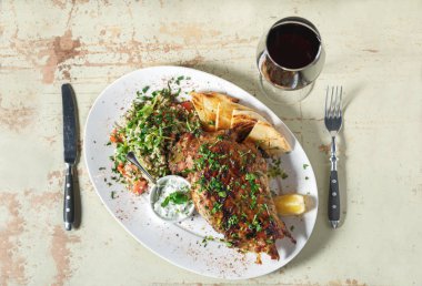 Pirinç bir garnitür ile beyaz tabak portre soslu kuzu budu pişmiş. Rustik ahşap masa ve bir kadeh kırmızı şarap.