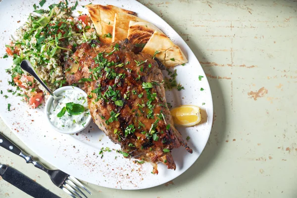 Pierna de cordero al horno con salsa en el plato blanco primer plano con un plato de arroz. Mesa de madera rústica y una copa de vino tinto . — Foto de Stock