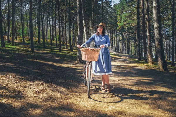 Kısa siyah saçlı ve şapka ayakta yakınındaki büyük chamomiles buket sepet ile bisiklet ile güzel genç gülümseyen kadın. Açık doğanın keyfini yaz kız. Yeşil arka plan.