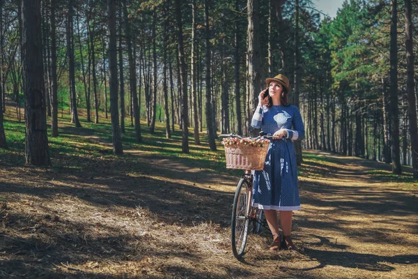 Kısa siyah saçlı ve şapka ayakta yakınındaki büyük chamomiles buket sepet ile bisiklet ile güzel genç gülümseyen kadın. Açık doğanın keyfini yaz kız. Yeşil arka plan.