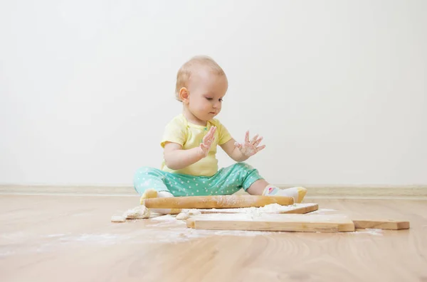 Маленькая милая девочка с головой сидит на полу, она сильно запачкана пшеничной мукой — стоковое фото