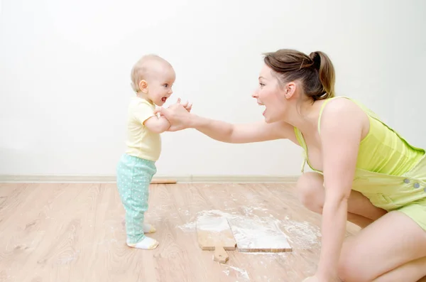 Красивая молодая мама и ее милая маленькая дочь играют. Дочь пытается съесть кусок сырого теста, мама держит ее за руку . — стоковое фото