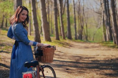 Kısa siyah saçlı ve şapka ayakta yakınındaki büyük chamomiles buket sepet ile bisiklet ile güzel genç gülümseyen kadın. Açık doğanın keyfini yaz kız. Yeşil arka plan.
