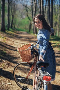 Kısa siyah saçlı ve şapka ayakta yakınındaki büyük chamomiles buket sepet ile bisiklet ile güzel genç gülümseyen kadın. Açık doğanın keyfini yaz kız. Yeşil arka plan.
