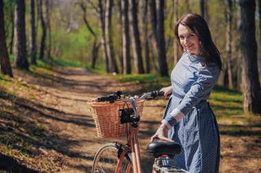 Kısa siyah saçlı ve şapka ayakta yakınındaki büyük chamomiles buket sepet ile bisiklet ile güzel genç gülümseyen kadın. Açık doğanın keyfini yaz kız. Yeşil arka plan.