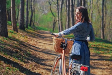 Kısa siyah saçlı ve şapka ayakta yakınındaki büyük chamomiles buket sepet ile bisiklet ile güzel genç gülümseyen kadın. Açık doğanın keyfini yaz kız. Yeşil arka plan.