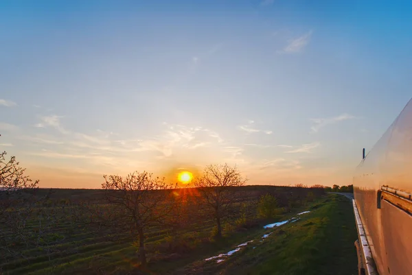 The sun sets over the horizon, the tops of trees in the clouds, View from the cab of the car at sunset and road.